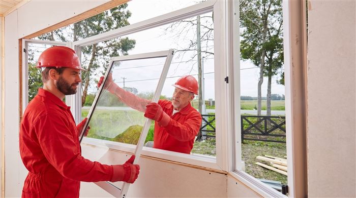 Two workers fitting a window into a framed opening